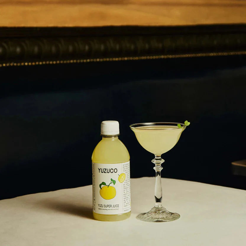 Yuzuco bottle and a cocktail with an herbal garnish on a table.